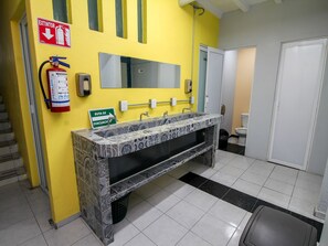 A bathroom with a yellow wall, a fire extinguisher, a hand dryer, a sink with a patterned countertop, and a toilet.