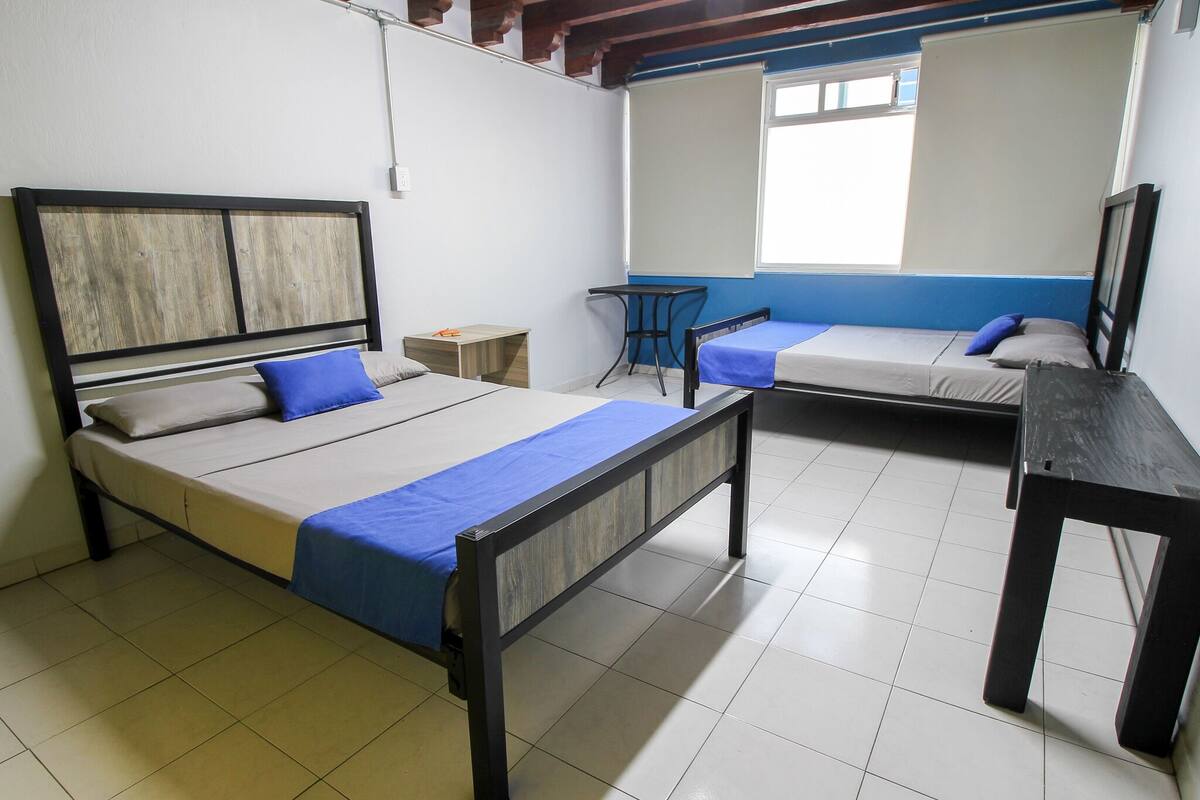 Een studentenkamer met twee bedden, een klein tafeltje en een raam.
