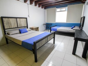 A dormitory room with two beds, a small table, and a window.