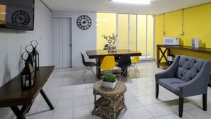 A dining area with a wooden table, chairs, a clock, a small plant, and a microwave on a shelf. - El Gran Hostal (Guadalajara)