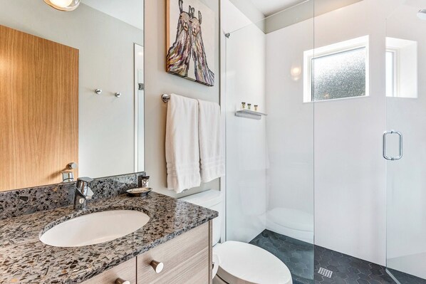 Un baño moderno con encimera de granito, dos lavamanos, cabina de ducha de cristal y un espejo grande.