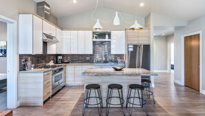 Una cocina moderna con una isla central, taburetes de bar, electrodomésticos de acero inoxidable e iluminación colgante.