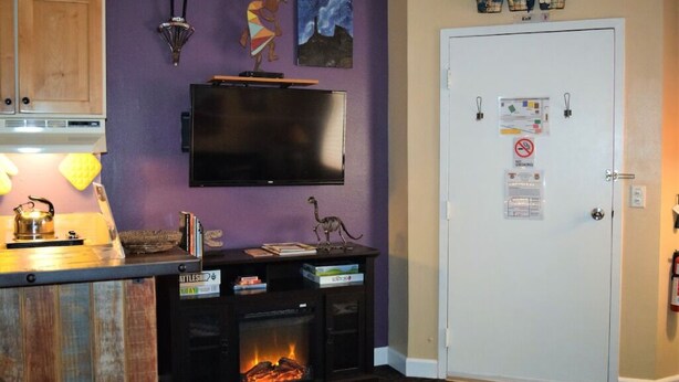 Un salon avec une cheminée, un téléviseur fixé au mur et une porte sur laquelle est accroché un tableau d’affichage.