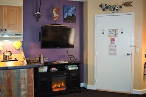 Una sala de estar con chimenea, un televisor montado en la pared y una puerta con un tablón de anuncios.