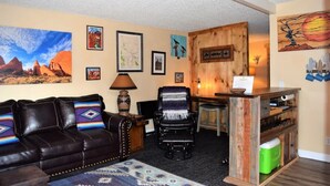 Un salon comprenant un canapé en cuir, un fauteuil, un bureau en bois et divers tableaux encadrés accrochés aux murs.
