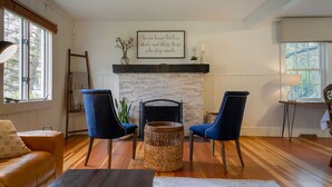 Ein Wohnzimmer mit Kamin, zwei blaue Sessel, einem Korbstuhl-Beistelltisch und einer Couch.