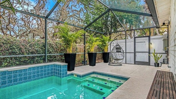Una piscina con cerramiento de vidrio, rodeada de plantas en macetas y árboles.