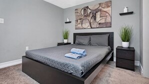 Un dormitorio moderno con una cama grande, paredes grises y un cuadro abstracto decorativo sobre ella.