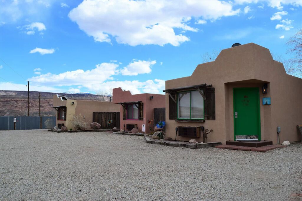 A row of adobe-style buildings with a gravel driveway, a green door, and a clear sky.