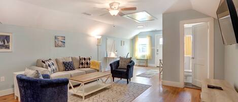 A spacious living room with hardwood floors, a ceiling fan, and a large window.