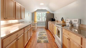 Una cocina con armarios de madera, encimera de granito, refrigerador, estufa y ventana con vista a follaje.