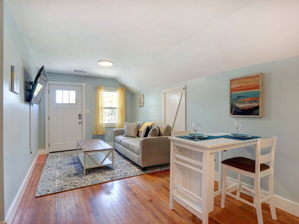 A compact living space with a sofa, a dining table with chairs, a small rug, and a painting on the wall. - Heated Pool Access, Large Tybee Home (Tybee Island)