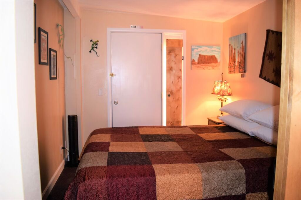 Quarto com colcha xadrez, luminária ao lado da cama e porta dando para outro cômodo.