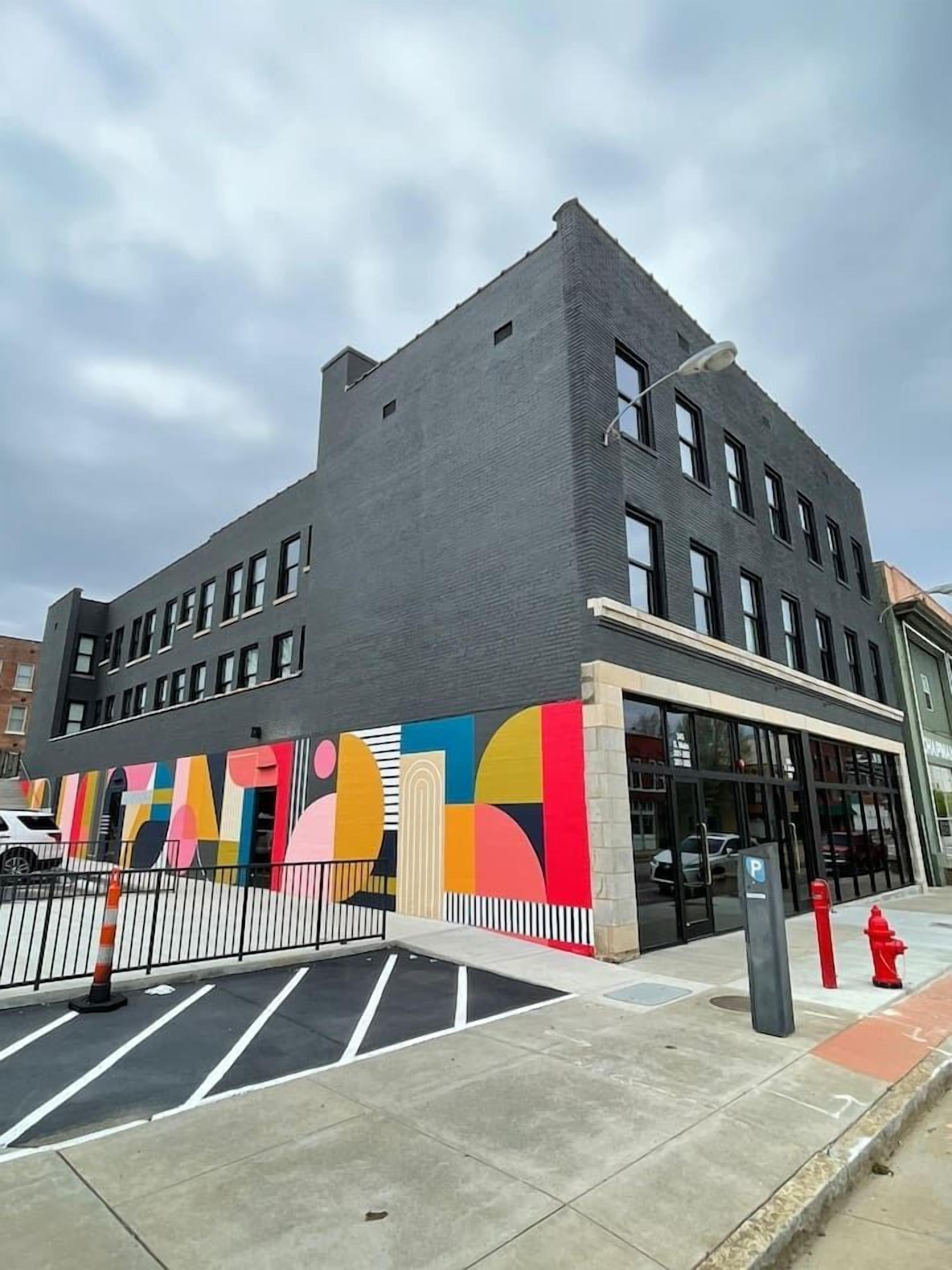 Un bâtiment moderne doté d’une grande entrée en verre et d’une fresque colorée sur le côté.