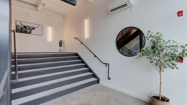 Un escalier avec des rampes noires, une plante en pot et un climatiseur fixé au mur.