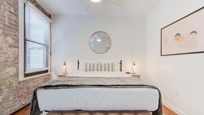 Une chambre avec un grand lit, un miroir rond, un mur en briques et un tableau encadré accroché au mur.