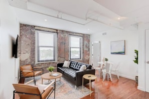 Relax in this stylish living room with a brick accent wall, large windows, and a comfortable sofa and armchair.