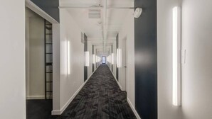Un pasillo largo y estrecho con alfombra estampada, paredes blancas y una puerta oscura al final.