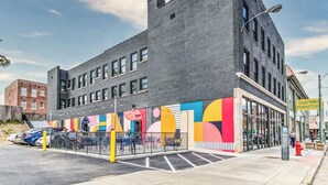 Un edificio moderno con facciata in mattoni, ampie finestre e un murale colorato sul lato.