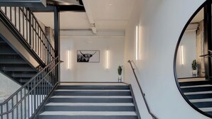 Una scala con ringhiere nere e gradini bianchi, che conduce a un pianerottolo con un quadro incorniciato e una pianta in vaso.