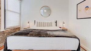 Une chambre à coucher avec un grand lit, deux tables de chevet avec des lampes, un grand miroir rond accroché au mur et un tableau encadré.