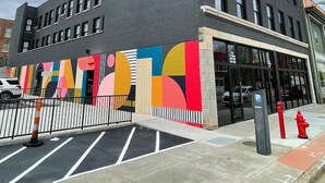 Un bâtiment moderne doté d’une grande entrée en verre et d’une fresque colorée sur le côté.