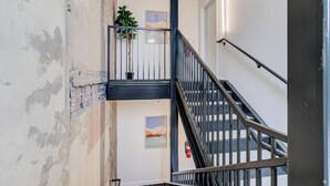Un escalier avec une rampe en métal, une plante sur la plateforme et un extincteur fixé au mur.