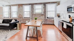 A modern kitchen with white cabinets, a stainless steel microwave, and a dishwasher. There is a dining area with a wooden table and white chairs. - Prime Downtown Hub | Walk to Beale, Culture & Eats (Memphis)