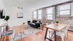 A modern living room with a black sofa, wooden coffee table, and a dining area with a wooden table and white chairs. - Prime Downtown Hub | Walk to Beale, Culture & Eats (Memphis)