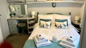 Une chambre à coucher comprenant un lit, deux tables de chevet, une commode, une coiffeuse et une étagère avec des objets décoratifs.