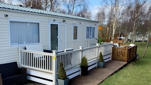 Une maison mobile dotée d’une terrasse clôturée, d’un petit porche et d’une porte d’entrée.