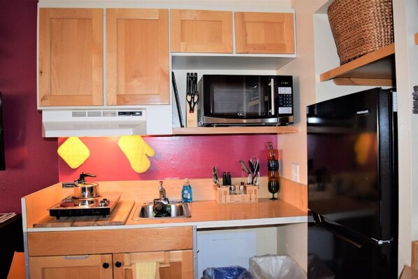 Une cuisine de taille réduite, dotée de meubles en bois, d’un four à micro-ondes, d’un réfrigérateur et d’une cuisinière à gaz.