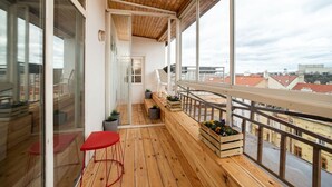 A balcony with wooden flooring, a red chair, and potted plants.