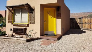 Un edificio de una sola planta con una puerta amarilla y un pequeño porche.