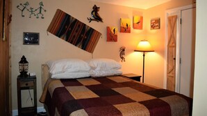 Un dormitorio con una cama grande, una mesita de noche con lámpara, y detalles decorativos en la pared, incluyendo una pintura de un pájaro y la silueta de un árbol.