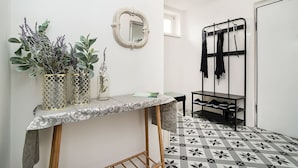 Un couloir avec un sol à motifs, un miroir, une composition florale et un porte-chaussures.
