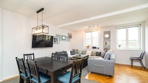 Un salon moderne avec une table à manger en bois foncé, des chaises rembourrées bleues, un canapé gris et un téléviseur à écran plat fixé au mur.