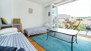 Une chambre à coucher de taille modeste, comprenant un lit, une petite table et un balcon offrant une vue sur les bâtiments et la verdure.