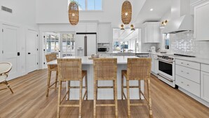 A spacious kitchen with white cabinets, a large island, wicker chairs, and pendant lights. - Luxury Dewey Beach Home, Private Beach Block, 4 Bed, 2.5 Bath, Park 3 Cars (Rehoboth Beach)