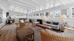 A spacious living room with a wooden dining table, wicker furniture, a fireplace, and large windows offering views of the outside. - Luxury Dewey Beach Home, Private Beach Block, 4 Bed, 2.5 Bath, Park 3 Cars (Rehoboth Beach)