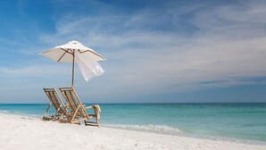 Ein Strand mit zwei Holzliegen und einem weißen Sonnenschirm.
