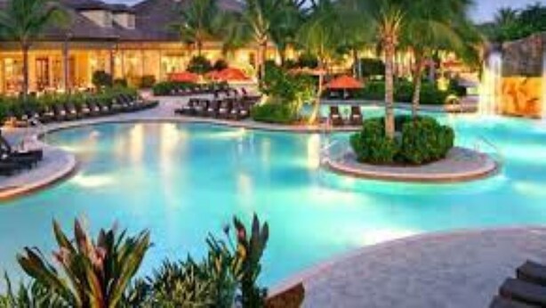 Ein Poolbereich eines Resorts mit Liegestühlen, Palmen und einem Gebäude mit Schwimmbecken.