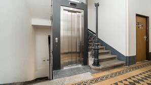 Ein Aufzug mit metallischer Oberfläche, einer Holztür und einer Treppe mit einem gemusterten Boden.