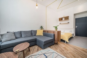 A modern living room with a grey sectional sofa, a wooden coffee table, and a bed with a yellow blanket. - Central designer studio by beautiful park & church (Prague)