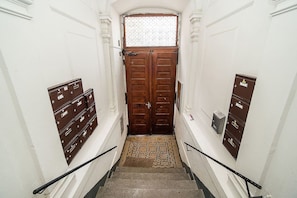 A narrow stairway with a patterned carpet leading to a wooden door with a window above. - Central designer studio by beautiful park & church (Prague)
