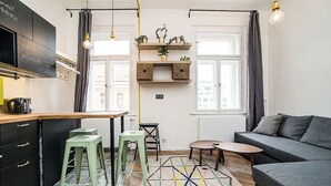 Ein kompakter Wohnbereich mit Küchenzeile, Sofa, Esstisch und einem gemusterten Teppich.