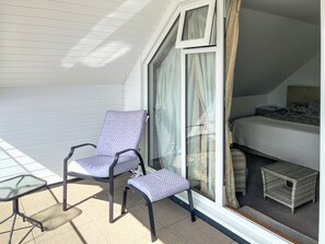 A balcony with a chair, a small table, and a bed with a headboard and pillows.