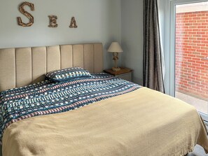 Una cama con una colcha estampada, un cabecero, una lámpara de noche y una pared con la palabra 'SEA' escrita.