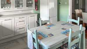 Eine Küche mit weißen Schränken, einem weißen Kühlschrank und einem Esstisch mit Stühlen.