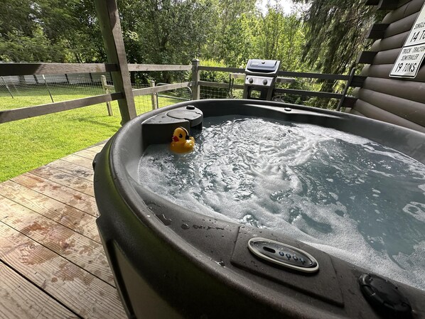 A hot tub with a duck, surrounded by a wooden deck and a fenced yard.
